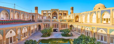 KASHAN, IRAN - OCTOBER 22, 2017: Panorama of the Agha Bozorg mosque with garden and madrasah on the ground floor, the beautiful portal and badgirs (wind towers) on the upper floor, on October 22 in Kashan. clipart