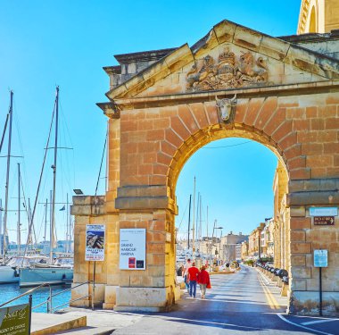 Birgu, Malta - 17 Haziran 2018: taş bull's head ile dekore edilmiş ve Kraliyet arması yukarıda geçen kemer, Xatt Il-Eşzamanla promenade, 17 Haziran'da Birgu içinde oyulmuş eski Bahriye (Tersane) geçit.