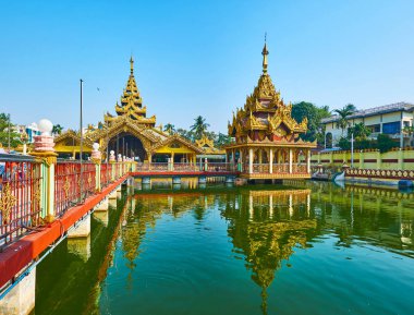 Explore Burmese landmarks, visiting Kyay Thone Pagoda, standing on the pond with system of bridges and ornate pavilions with pyatthat roofs and carved details, Yangon, Myanmar. clipart