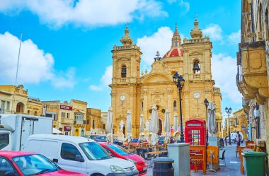 Xaghra, Malta - 15 Haziran 2018: Birçok park edilmiş arabalar ve 15 Haziran Xaghra açık hava kafeleri ile meşgul Meydanı'na Nativity Basilica üzerinde görünümü.