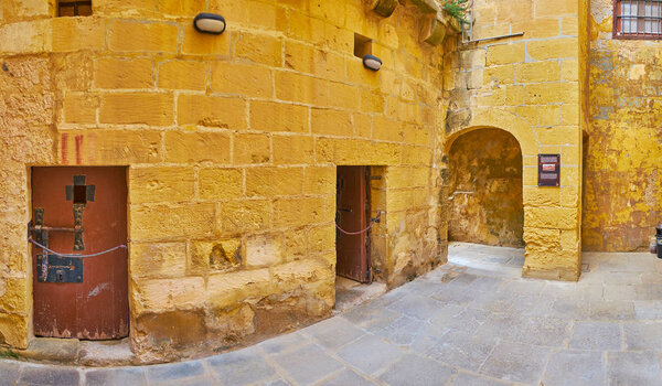 VICTORIA, MALTA - JUNE 15, 2018: The stone courtyard of Old Prison with massive wooden doors of the cells, Rabat Citadel, on June 15 in Victoria.