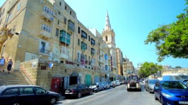 Valletta, Malta - 19 Haziran 2018: Turistik tramvay sürücüler Marsamxett cadde boyunca geleneksel Malta yaşam yapılardır ve çan kulesi St Paul Anglikan Pro-Cathedral, Haziran 19 Valletta manzaralı