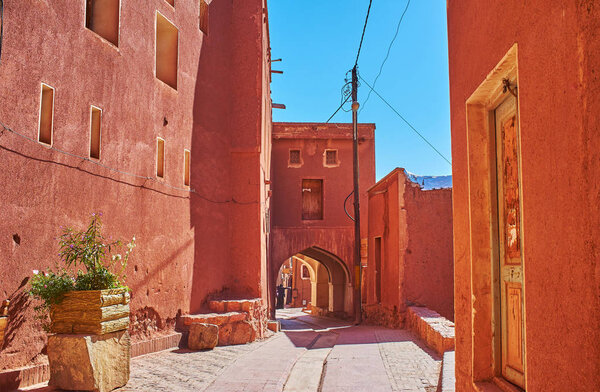 Walking down the old street with a view on reddish buildings and the ancient Harpak Fire Temple - the oldest monument in Abyaneh village, Iran.