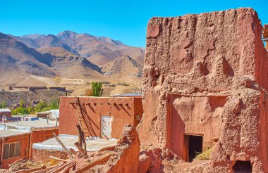 Yıkık kırmızı adobe bir terasta yer Abyaneh köy pitoresk Karkas dağlar ve antik kale arka planda, Iran ile bina terk.