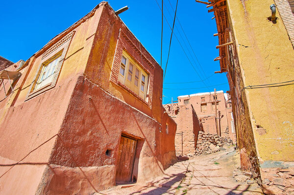 The steep ascent street in medieval mountain village with red adobe houses on both sides, Abyaneh, Iran.
