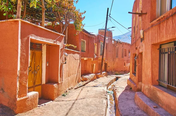 The old street of Abyaneh village with deep gutter in earthen road and preserved reddish buildings, Iran.