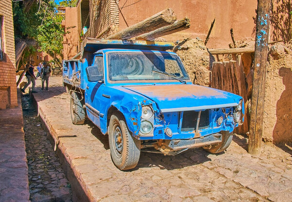 ABYANEH, IRAN - OCTOBER 23, 2017: The vintage damaged pickup rides the narrow steet of the village, carrying the old logs, on October 23 in Abyaneh