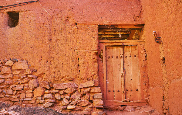 The old house wall, built partly of stone and earthen brick and covered with reddish adobe, Abyaneh, Iran.