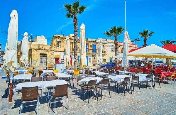 MARSAXLOKK, MALTA - JUNE 18, 2018: The seaside promenade of the village is occupied with tourist cafes and cozy restaurants, popular among the holidaymakers, on June 18 in Marsaxlokk.