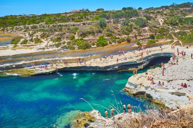 Marsaxlokk, Malta - 18 Haziran 2018: Tatilciler güneşlenme, yüzme ve Marsaxlokk 18 Haziran tarihinde St Peter's havuzu - Delimara kenarı, şaşırtıcı kireçtaşı plaj şnorkel tadını çıkarın.