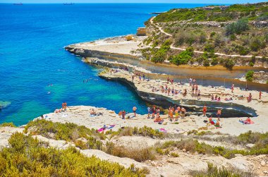Marsaxlokk, Malta - 18 Haziran 2018: St Peter's havuzu ve 18 Haziran Marsaxlokk içinde ve etrafında kalabalık plaj manzaralı Delimara Pennsula üzerinden Akdeniz deniz manzarası.