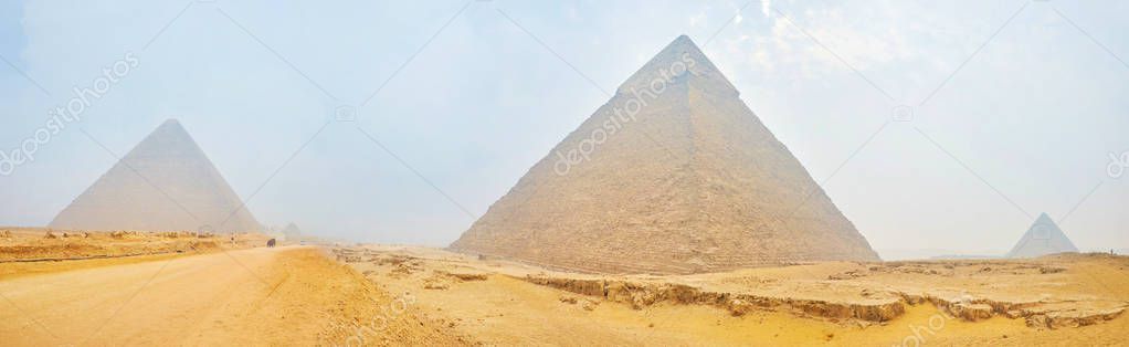 Panorama of ancient Pyramids, surrounded by sands of Sahara desert and covered with winter haze, archaeological site of Giza Necropolis, Egypt.