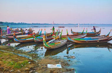 AMARAPURA, MYANMAR - FEBRUARY 21, 2018: The colorful wooden canoes weit the tourists in port on Taungthaman Lake and offers sunset trip to U Bein Bridge, on February 21 in Amarapura.