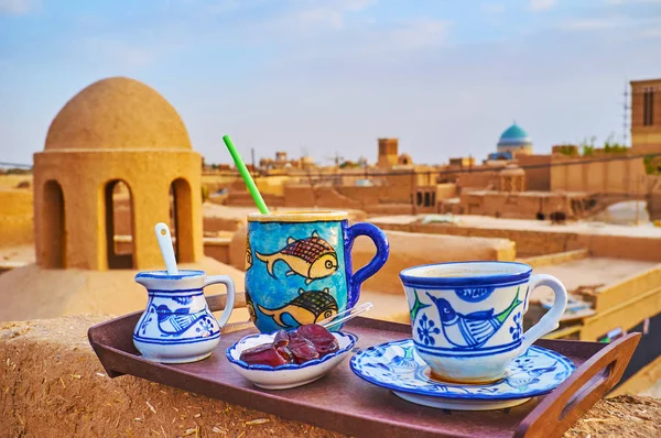 Enjoy the lunch or coffee break on medieval adobe roof of traditional cafe, offering tea, coffee and sweet dates from handmade cups and mugs, decorated with primitive animalistic patterns, Yazd, Iran.