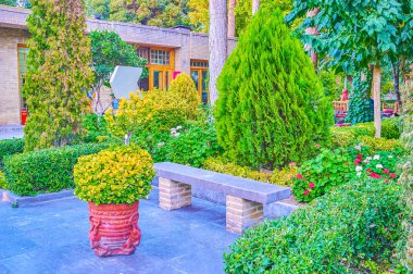 ISFAHAN, IRAN - OCTOBER 19, 2017:  The cozy stobe bench among lush amazing greenery in Chehel Sotoun complex, on October 19 in Isfahan