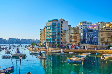 ST JULIANS, MALTA - JUNE 20, 2018: Enjoy the view on Spinola Bay with numerous moored boats and curved seaside promenade of George Borg Olivier, on June 20 in St Julians.
