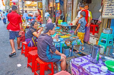 YANGON, MYANMAR - FEBRUARY 17, 2018:   Locals enjoy the dinner in small outdoor cafe in Chinatown market, on February 17 in Yangon.