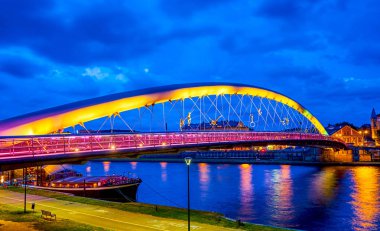 Renkli akşam aydınlatma modern babası Bernatek yaya köprüsü ve demirli büyük tekne restaurant üzerinde Vistula Nehri, Krakow, Polonya