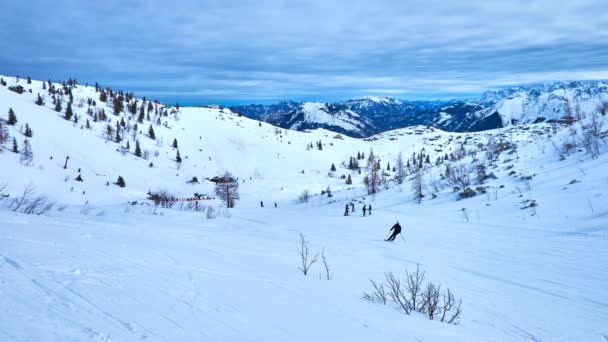 重い雲の Feuerkogel 斜面多数ゲレンデとアルプスの大規模なダッハシュタインのスキーヤー スノーボーダーとスケートスノーシュー オーストリアのザルツカンマーグートで Ebensee のリゾートを訪れるの — ストック動画