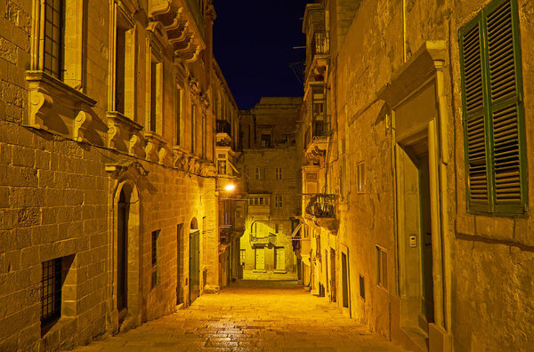 Illuminated quiet hilly street, lined with old stone edifices, Valletta, Malta.