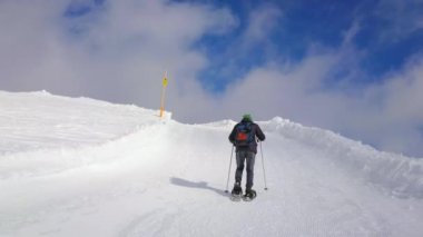 Snowshoer yavaş yavaş yokuş yukarı yürür Dachstein-Krippenstein üst iz üzerinde dik bir yamaç boyunca snowdrifts ile hızlı çalışan bulutlar tepenin Salzkammergut, Avusturya kaplı.