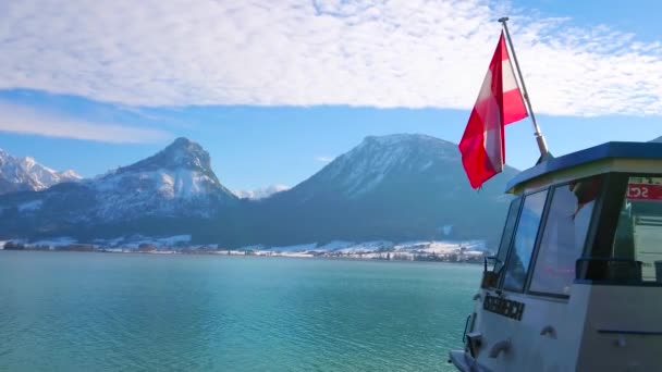 ヴォルフガング オーストリア 2019 明るい青い波状の表面聖ヴォルフガングの 対岸にフェリーの船尾および岩が多いアルプスのオーストリアの国旗を振ってヴォルフガング湖 — ストック動画