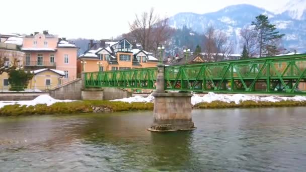 高速流れるトラウン川を渡る古い橋の景色 その銀行の風光明媚な邸宅 背景には雪のアルプス 悪いバートイシュル ザルツカンマーグート オーストリア — ストック動画