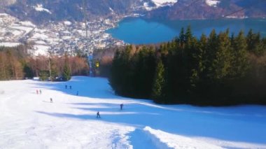 Zwolferhorn dağ yamacında teleferik muhteşem görünümü, kayakçılar, yokuş yukarı gidiyor, kozalaklı orman, Alpler ve vadide derin mavi Wolfgangsee gölü, St Gilgen, Salzkammergut, Avusturya.