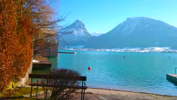 ヴォルフガングゼーのアズール波紋の海と湖の後ろのラベンベルクとピッシェンベルク山脈の風光明媚な風景 セントヴォルフガング ザルツカマーグート オーストリアの湖畔の小さなベンチ — ストック動画
