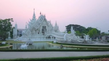 Görkemli Beyaz Tapınak (Wat Rongkhun) süslü köprü, heykeller, heykeller, ayna desenleri, kabartma dekorlar ve alacakaranlık, Chiang Rai, Tayland küçük bir göl ile