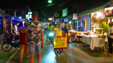 Pai, Tayland - 5 Mayıs 2019: Walking Street'te çok sayıda yiyecek ve hediyelik eşya tezgahı, kafe, bar ile kalabalık Gece Pazarı; sepeti ile sokak satıcısı ev hindistan cevizi dondurma, 5 Mayıs'ta Pai sunuyor