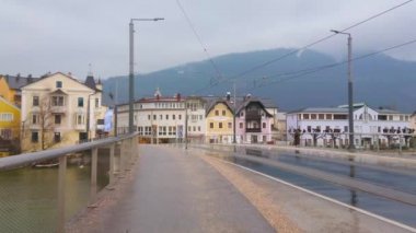 Gmunden, Avusturya - 22 Şubat 2019: Issız Traun köprüsü (Traunbrucke) boyunca giden kırmızı tramvay, 22 Şubat'ta Gmunden'de karanlık yolda su birikintilerinde yansıtılır.