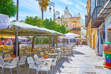 SANLUCAR, SPAIN - 22 Eylül 2019: 22 Eylül 'de Sanlucar' da Plaza del Cabildo Meydanı 'nda yer alan açık hava kafelerinin masaları ve güneşlikleri boyunca uzanan ara sokak
