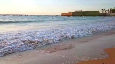 Santa Catalina Ortaçağ kalesi ve İspanya 'nın Cadiz şehrinde küçük balıkçı tekneleri filosuyla alacakaranlık La Caleta sahilinde dalgalar.