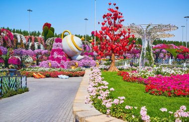 DUBAI, BAE - 5 Mart 2020: Mucize Bahçesi geçidinde yürüyün ve manzaranın tadını çıkarın - asılı kalpleri, dev güneş gözlükleri ve çaydanlığı olan aşk ağacı Petunya çiçek tarhının ortasında, 5 Mart 'ta Dubai' de