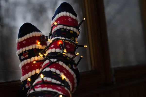 Sıcak beyaz ışıklar ve ayak Noel çorap yol açtı. Geç akşam evde kız rahatlatıcı. Kış tatil Noel ve yeni yıl kavramı. Pencere tarafından yün çorap ayak.