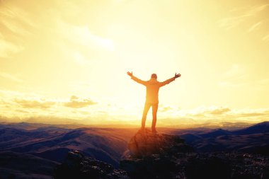 Traveler hiker stands raised arms against mountains