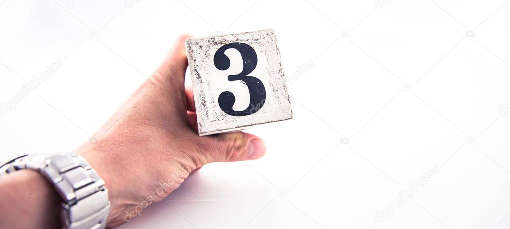 A hand holding digit number 3 (three) on white background