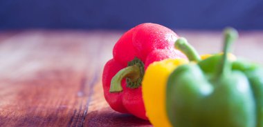 Eski ahşap masada kırmızı, sarı ve yeşil biber.