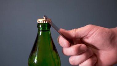 Adam şişeyi özel bir açıcıyla köpüklü içecekle açıyor. Metal kapaklı cam şişe.