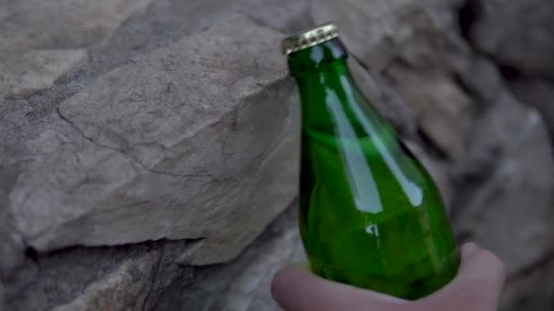 Een man opent een fles koolzuurhoudende drank slaan de stoeprand. Glazen fles met metalen deksel — Stockvideo