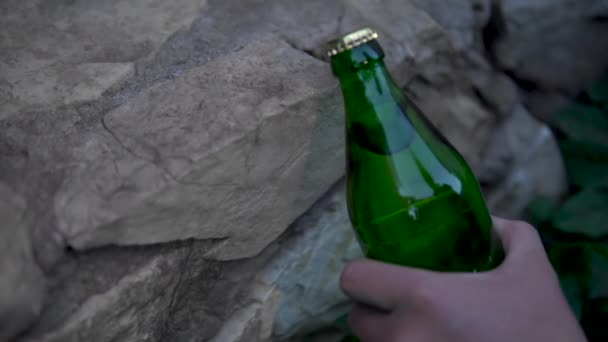 A man opens a bottle of carbonated drink hitting the curb. Glass bottle with metal lid — Stock Video