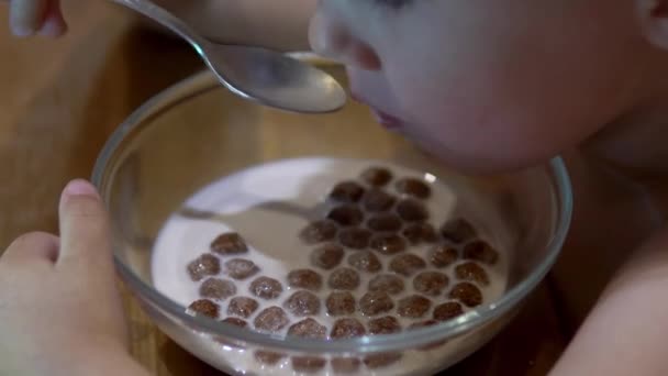 Ребенок ест шоколадные шарики с молоком и смотрит мультики — стоковое видео