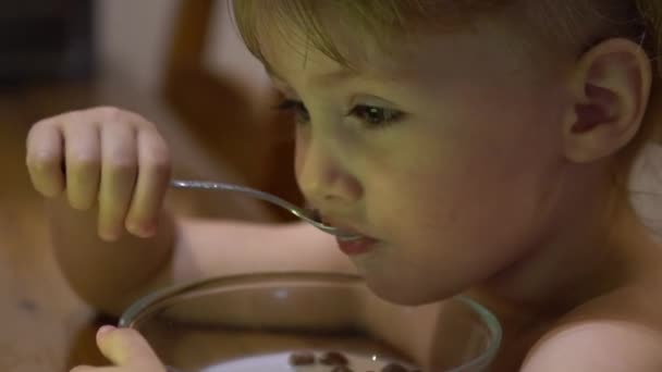 Ett barn äter chokladbollar med mjölk och tittar på tecknade serier — Stockvideo