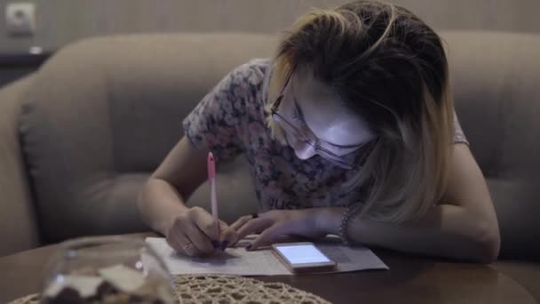La chica escribe en las notas del cuaderno. Sentado en la sala de estar a la mesa — Vídeo de stock