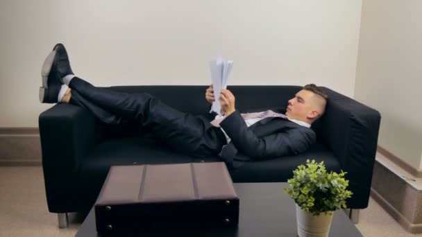 Бізнесмен лежить на дивані і читає документи — стокове відео