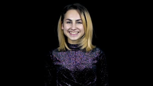 Een jonge vrouw glimlachend staat in een avondjurk op een zwarte achtergrond. Confetti klapper shot valt op hoofd. Slow Motion — Stockvideo