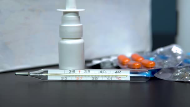 En kvinna tar termometern. Medicinering på bordet. Flerfärgade piller för behandling av sjukdomar ligger på bordet — Stockvideo