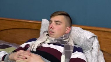 Ağzında termometre olan genç bir adam. Termometredeki sıcaklığı kontrol eder ve sıcaklığın normale dönmesine sevinir. Closeup