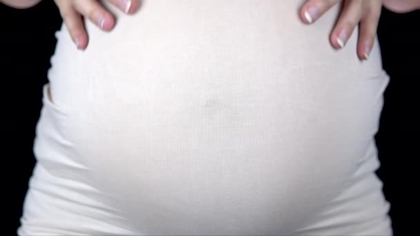 Pregnant woman stroking her stomach and showing a heart from hands. Woman in a light T-shirt — Stock Video